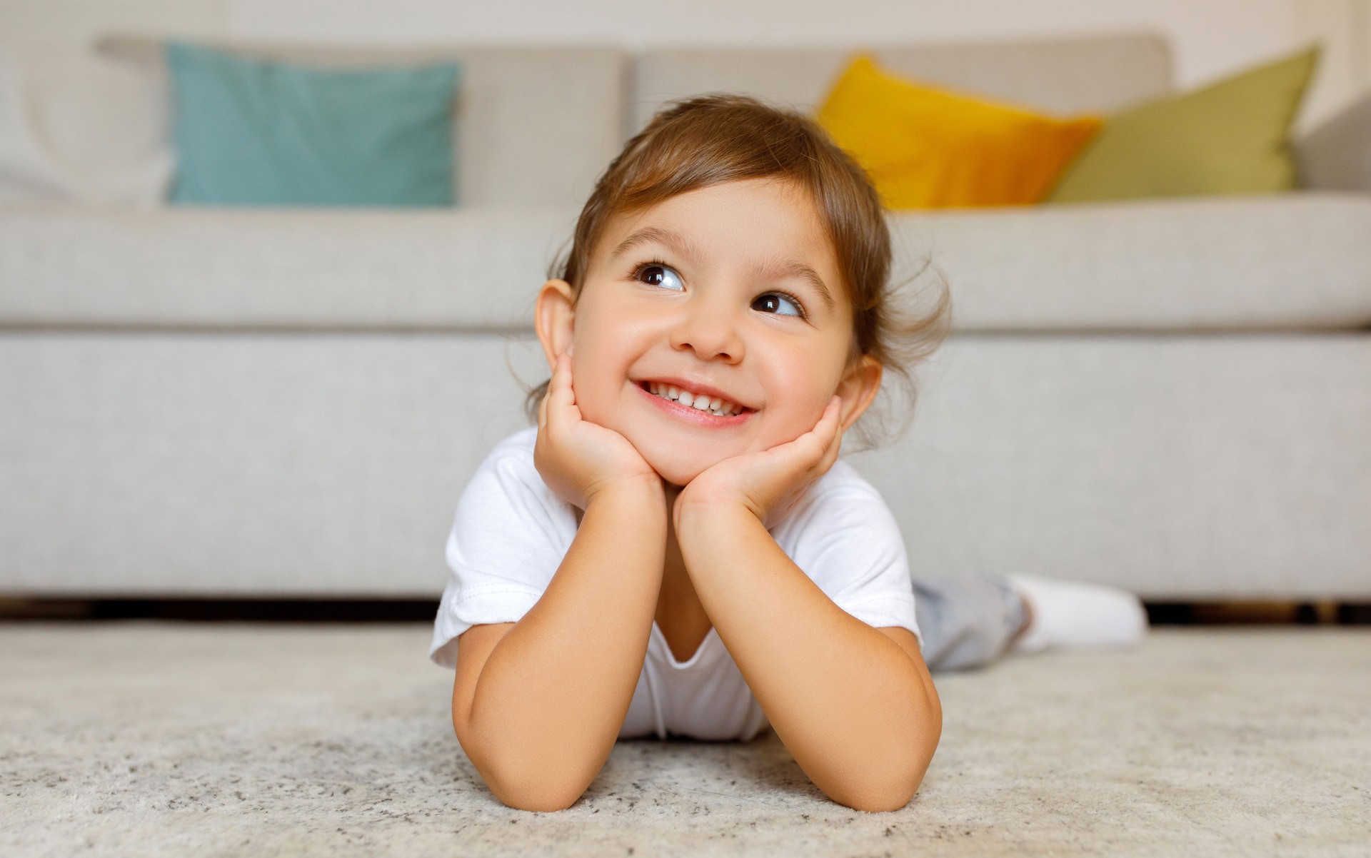 Cheerful cute little girl daydreaming on the floor at home